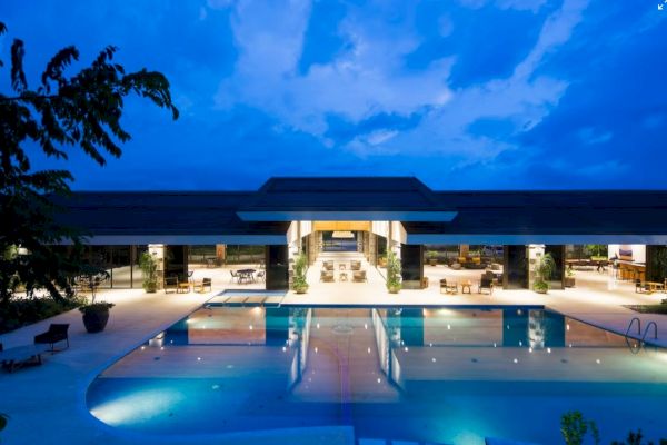 A luxurious, modern building with large, open spaces is seen at night, featuring an illuminated swimming pool in the foreground.