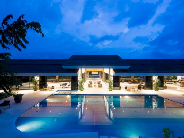 A luxurious, modern building with large, open spaces is seen at night, featuring an illuminated swimming pool in the foreground.