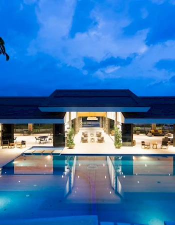 A luxurious building with an extensive pool and bright lights sets against a dramatic evening sky backdrop.