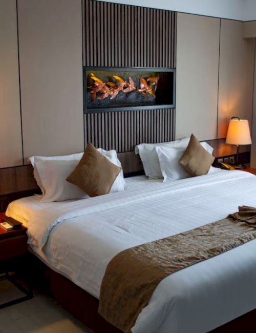 A well-lit hotel room featuring a large double bed, bedside lamps, decorative pillows, and curtains on the window, providing a cozy atmosphere.