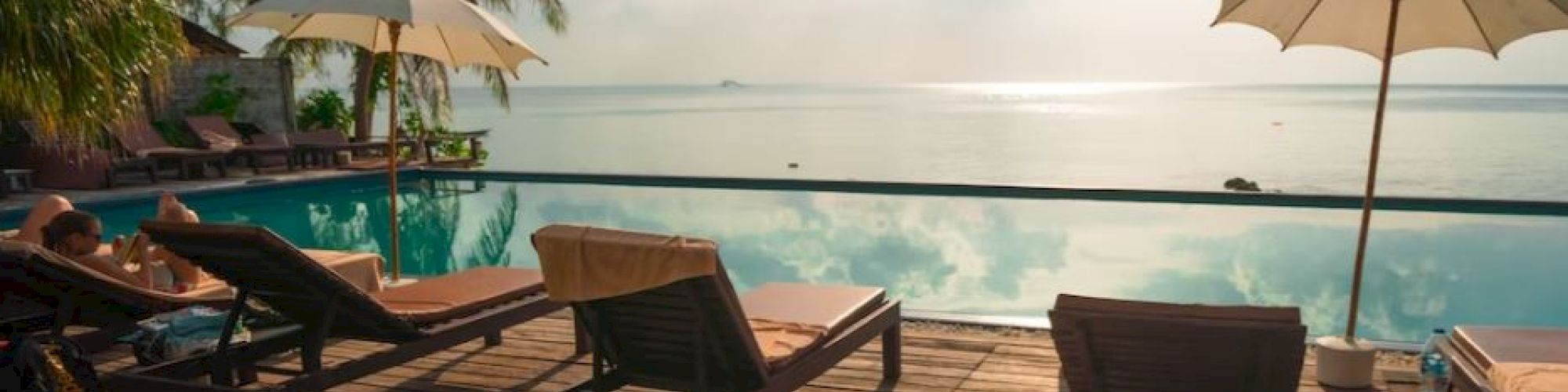 The image shows a serene poolside area with lounge chairs and umbrellas, overlooking a calm ocean under a partly cloudy sky.