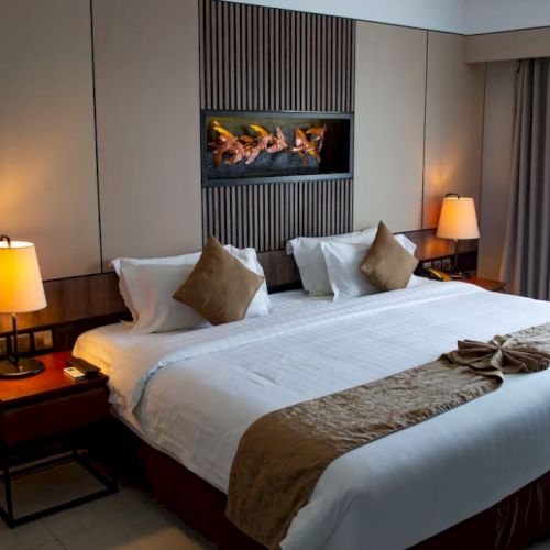 A neatly arranged hotel room with a large bed, bedside lamps, artwork on the wall, and a window with closed curtains.