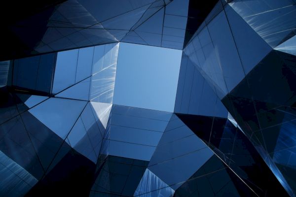 A complex architectural structure featuring reflective glass surfaces with an open view of the sky at the center.