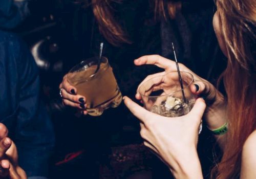 Individuals are socializing, holding drinks, and laughing in a lively environment, likely a party or a club.