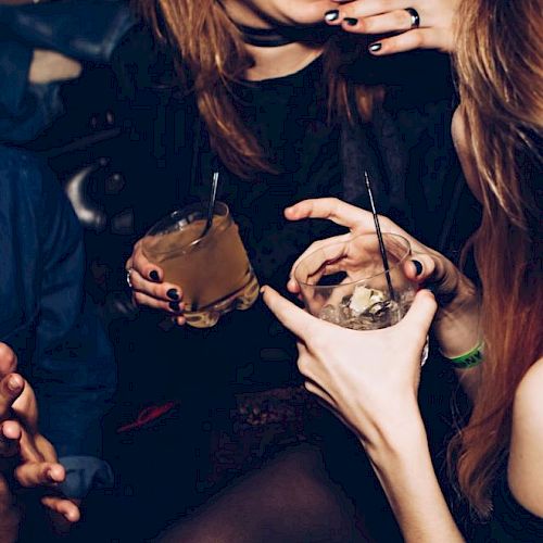 Individuals are socializing, holding drinks, and laughing in a lively environment, likely a party or a club.