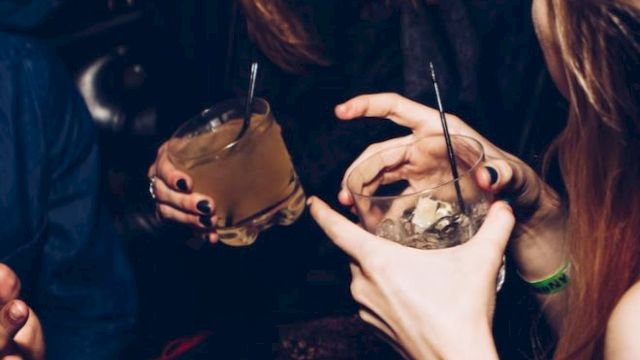 Individuals are socializing, holding drinks, and laughing in a lively environment, likely a party or a club.