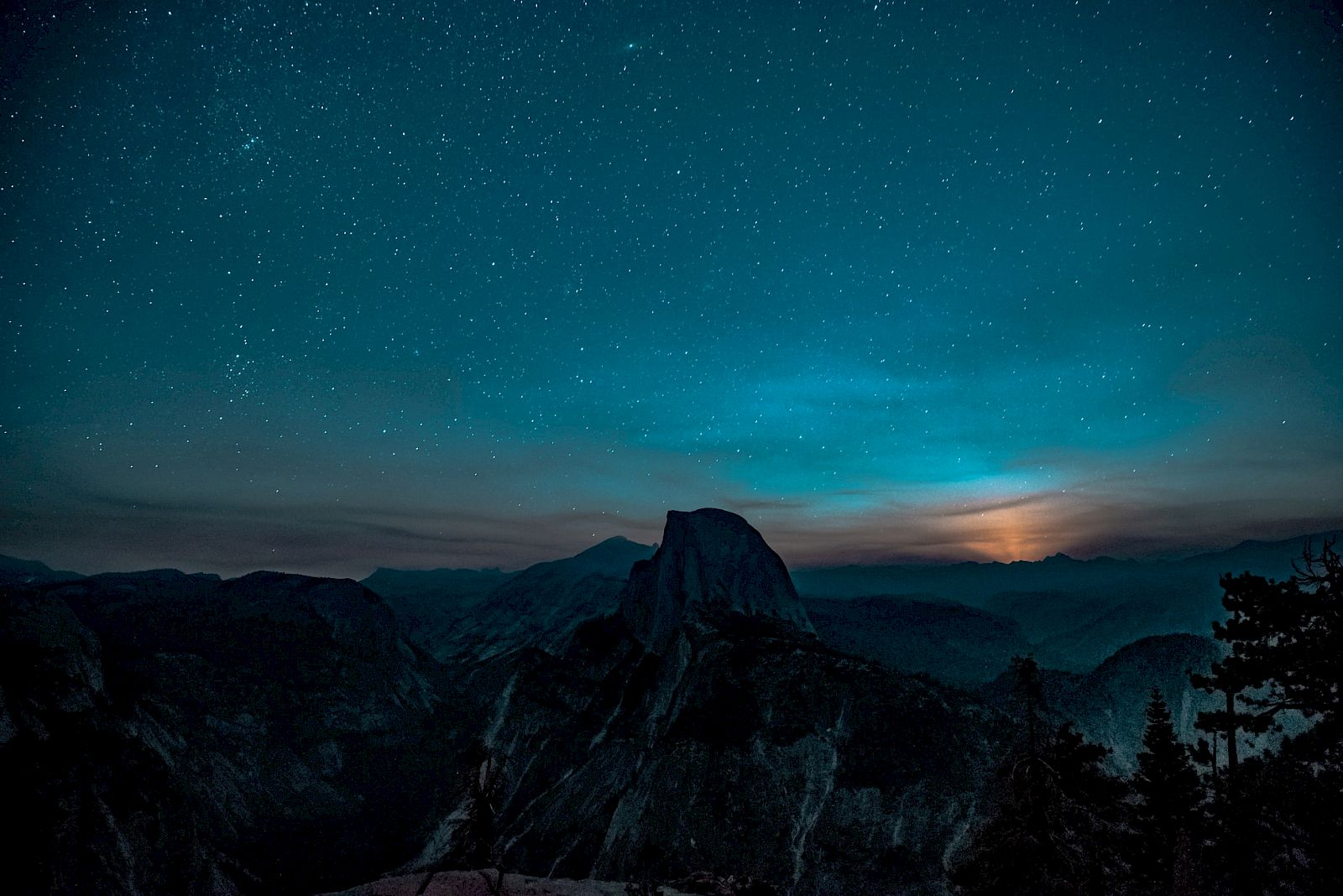 A star-filled night sky, with distant hills silhouetted against the faint glow of the setting sun or rising moon, creating a serene scene.