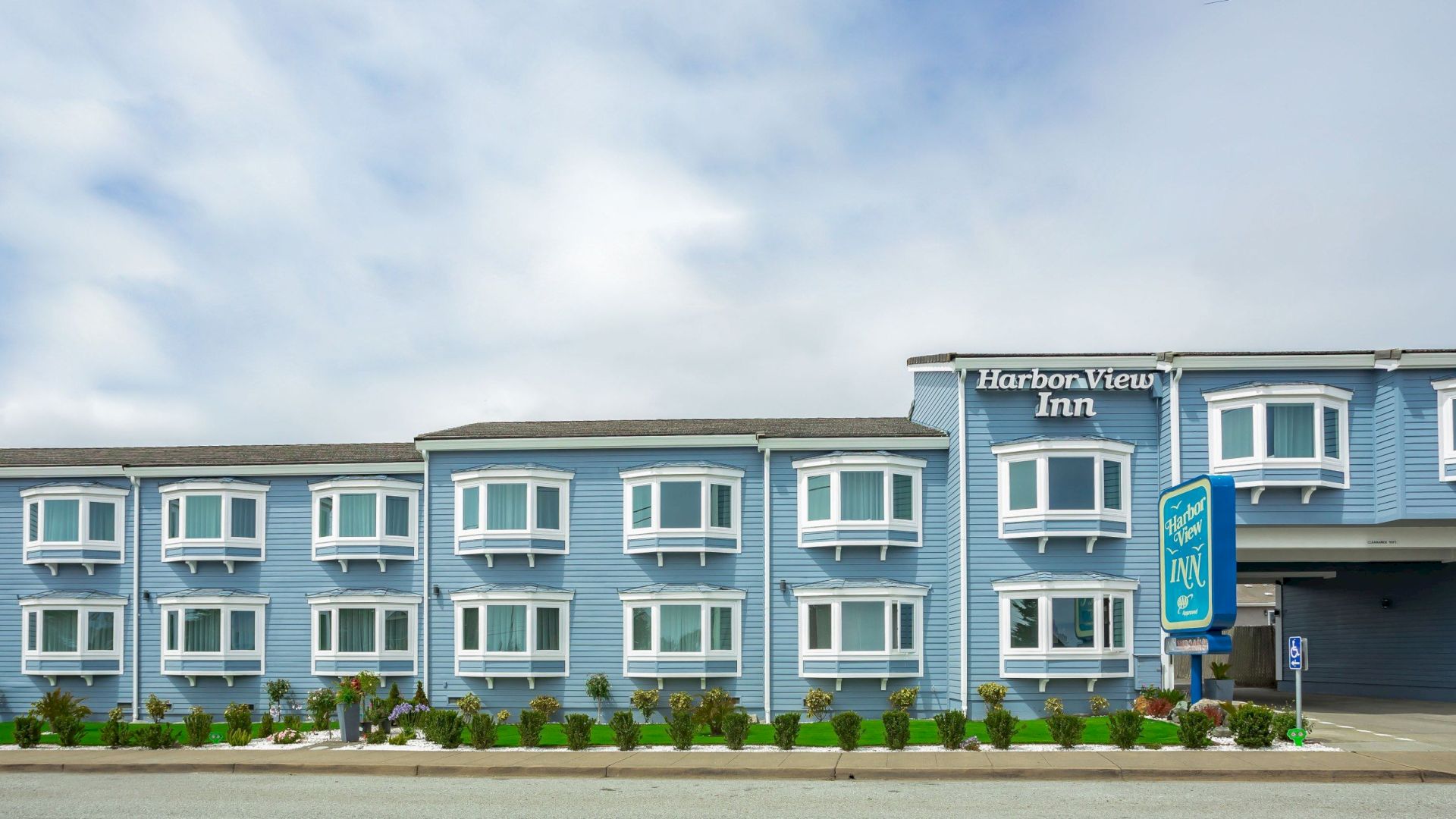 The image shows a blue building labeled "Harborview Inn" with white-framed windows, a roadside in front, and a sign indicating the inn's name.