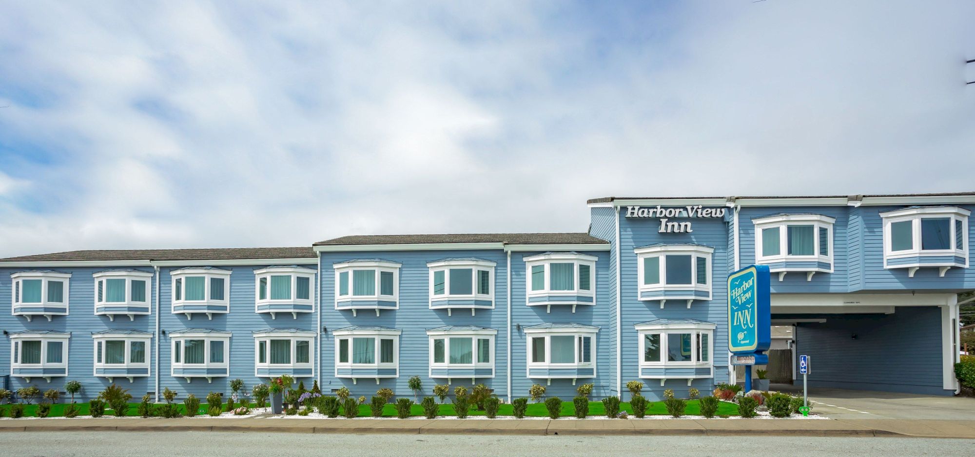 The image shows a blue building labeled "Harborview Inn" with white-framed windows, a roadside in front, and a sign indicating the inn's name.