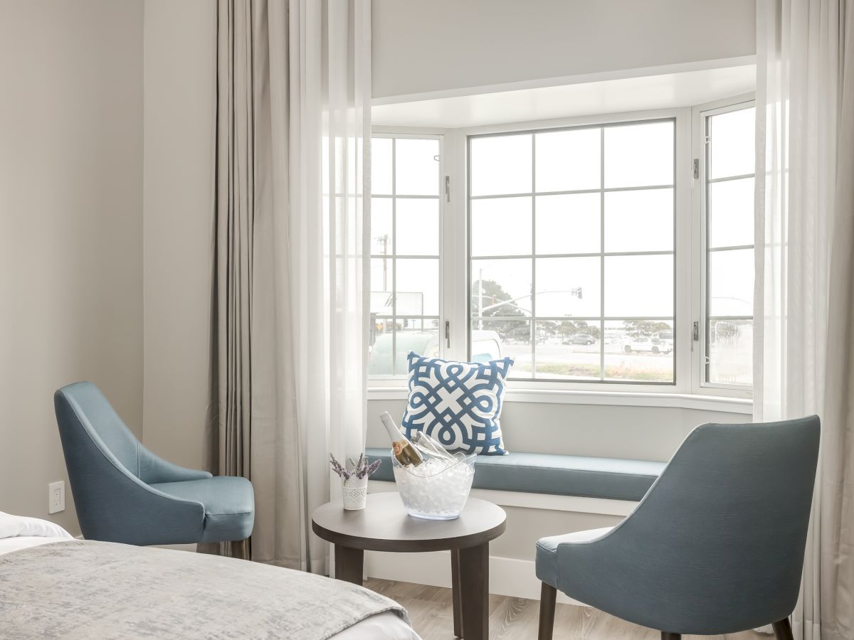 A cozy, modern sitting area with two blue chairs, a small round table, and a bay window seat adorned with a decorative blue pillow.