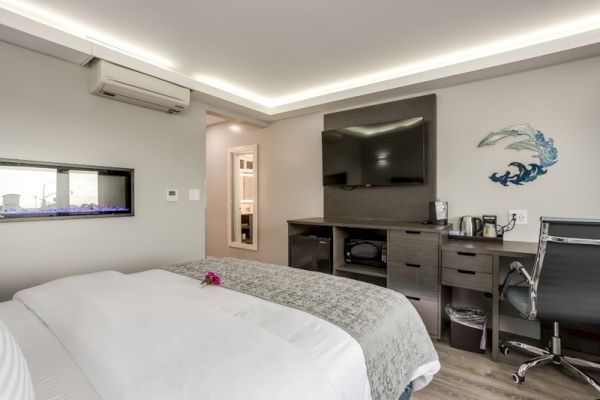 A modern bedroom with a large bed, TV, desk, chair, and wall art. The room has stylish lighting and an air conditioner.