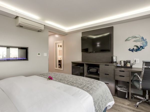 A modern bedroom with a large bed, TV, desk, chair, and wall art. The room has stylish lighting and an air conditioner.