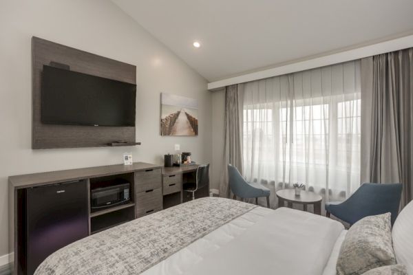 A modern hotel room featuring a bed, flat-screen TV, artwork, curtains over a large window, a desk, two chairs, and a small round table.