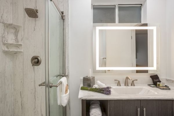 A modern bathroom with a shower, illuminated mirror, sink, countertop items, and fresh towels.