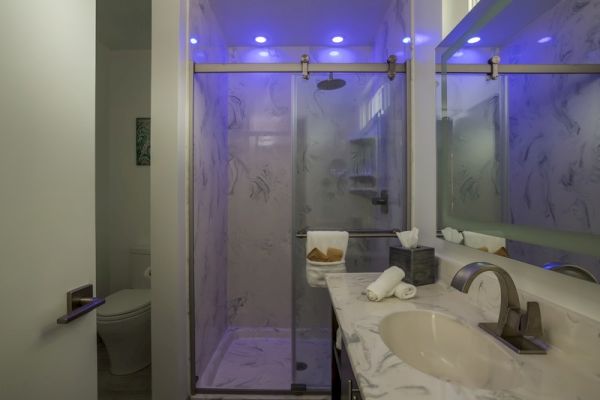 A modern bathroom with a marble sink, a glass shower enclosure illuminated by blue LED lights, and a toilet tucked in the corner, ending the sentence.