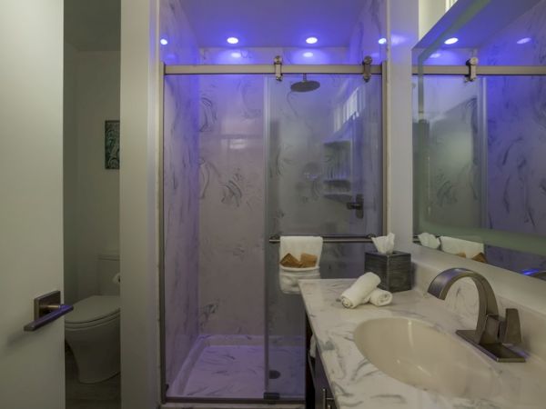 A modern bathroom with a marble sink, a glass shower enclosure illuminated by blue LED lights, and a toilet tucked in the corner, ending the sentence.