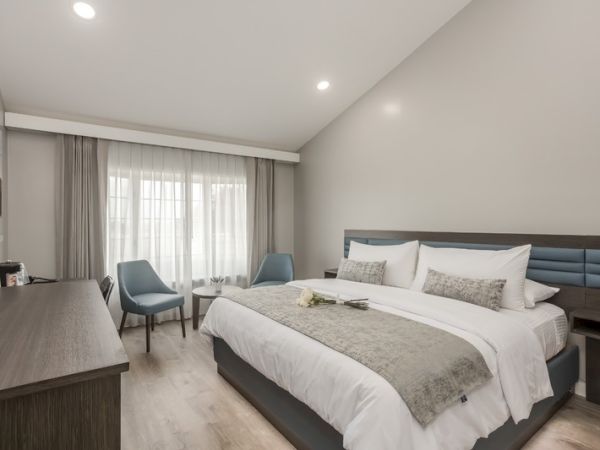 A neatly arranged hotel room with a large bed, two chairs, a side table, and a desk with amenities, all in a modern and clean design.