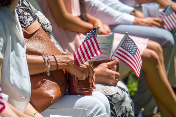 People seated, holding small American flags, possibly during a patriotic event or ceremony, with sunlight highlighting the scene.