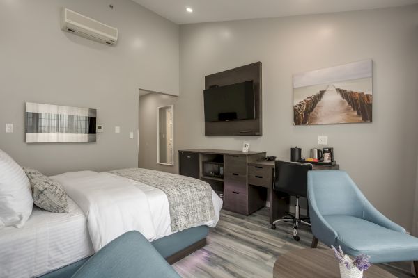 A modern hotel room with a bed, TV, desk, chair, and wall art. The setup includes a coffee maker and well-arranged seating.