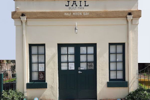 An old jail building from 1919 in Half Moon Bay, with double doors, two windows, and minimal signage.