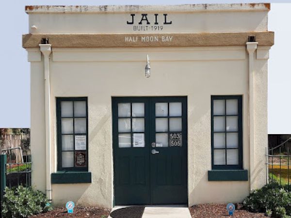 An old jail building from 1919 in Half Moon Bay, with double doors, two windows, and minimal signage.