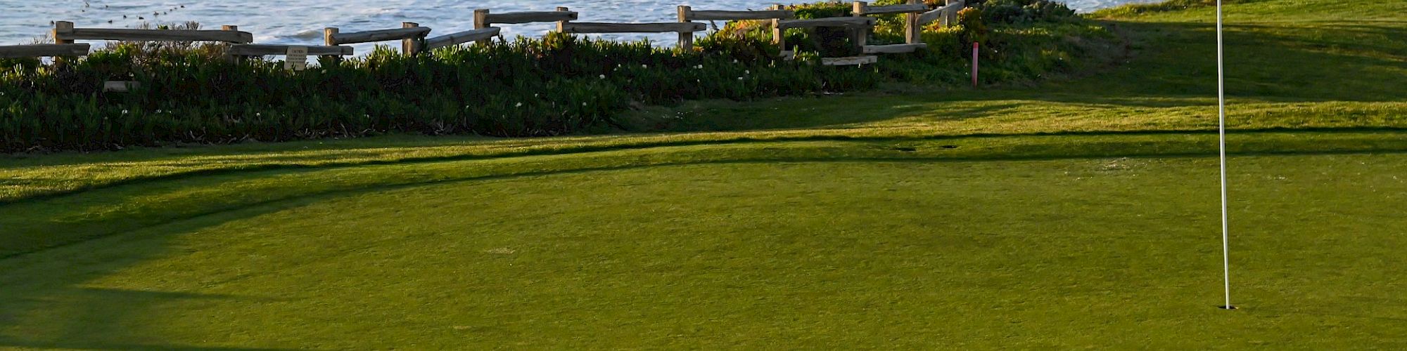 The image shows a golf course by a rocky coastline with a blue flag near a green, waves crashing and cliffs in the background, ending the sentence.