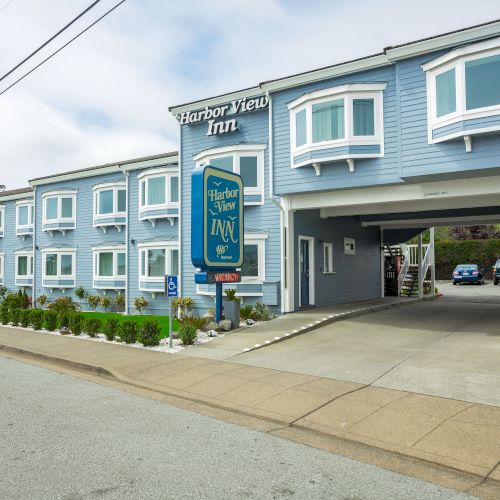 Image shows the exterior of Harbor View Inn, a blue building with multiple windows and a driveway entrance, along with a sign by the road.