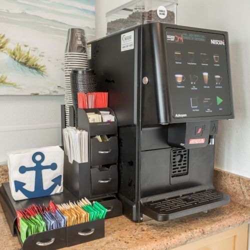 The image shows a coffee machine with various options and a stand holding cups, stir sticks, sugar packets, and creamers on a countertop, ending the sentence.