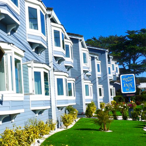 The image shows a blue building with multiple box windows, a lush lawn, and a sign reading 