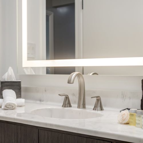 A modern bathroom sink setup with a lit mirror, faucet, tissue box, towels, 