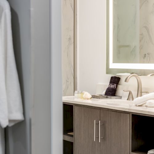 The image shows a bathroom view through a doorway, featuring a sink, mirror, and a robe hanging on the left side.