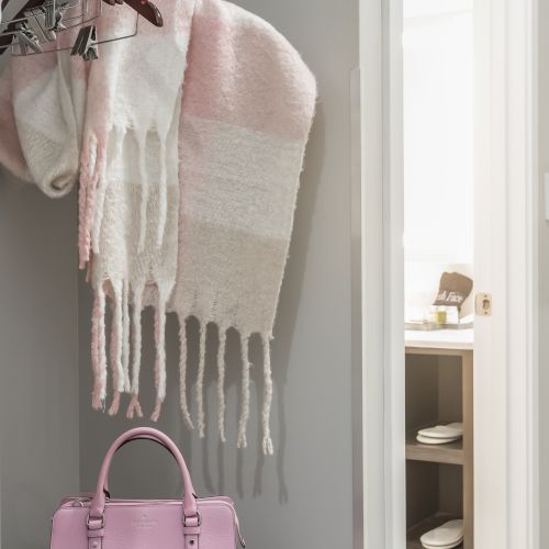 A closet containing hangers with scarves and a pink handbag. The doorway leads to another room with shelves.