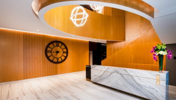 A modern lobby with a marble reception desk, wooden accents, a large wall clock, and elegant lighting fixtures.