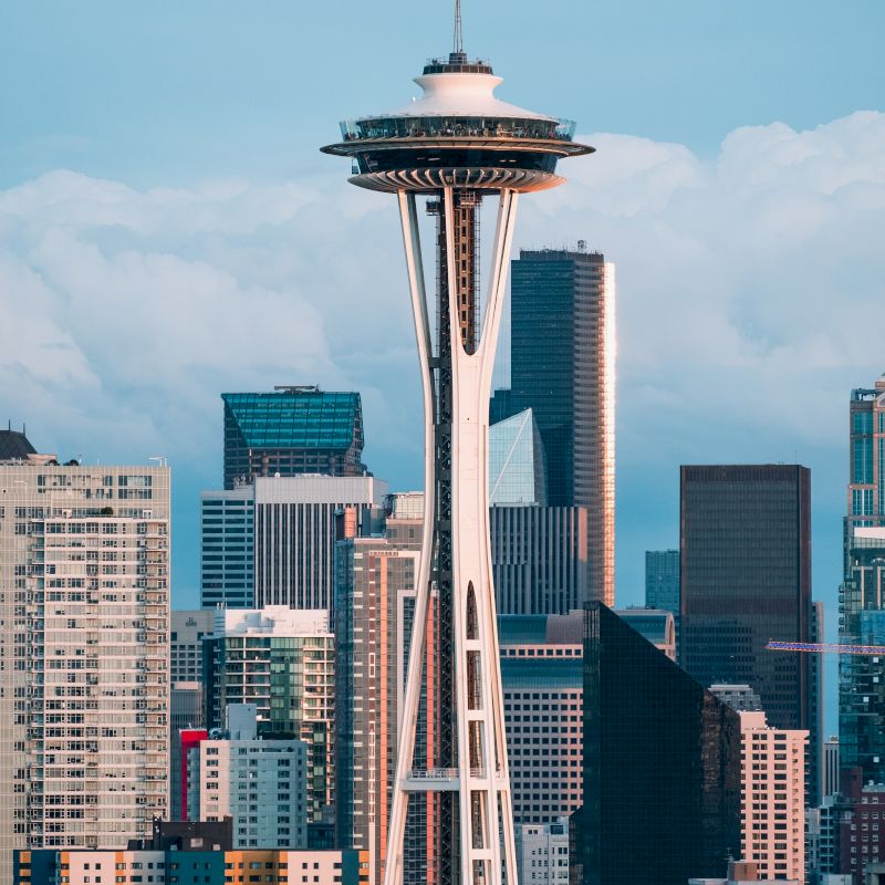 The image shows the Space Needle with downtown Seattle's skyline in the background, featuring various modern skyscrapers.