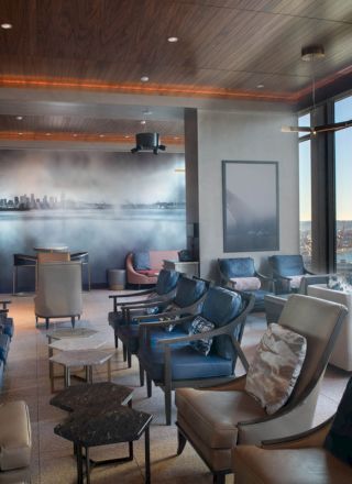 A modern lounge with comfortable seating, large windows offering a scenic view, and a mural of a city skyline on the back wall.