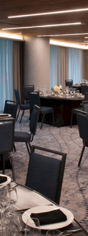 A formal dining room with round tables set with plates, glasses, and napkins arranged, ready for an event or banquet, with dim lighting.