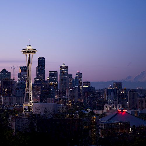 City skyline at twilight with a prominent observation tower and mountain in the background.